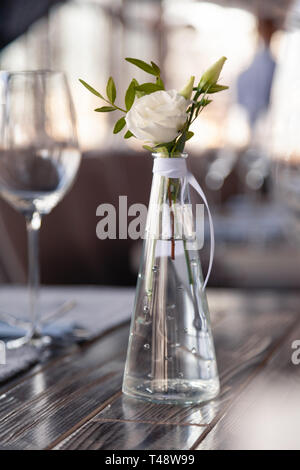 Transparentes Glas Vase mit Blumenstrauß vor Hintergrund der Tabelle Einstellung im modernen Restaurant. Wein und Wasser Gläser stehen in der Zeile auf Holz Stockfoto