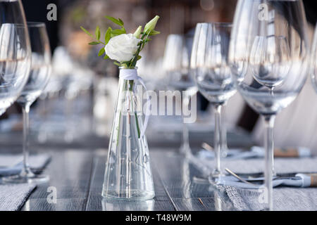 Transparentes Glas Vase mit Blumenstrauß vor Hintergrund der Tabelle Einstellung im modernen Restaurant. Wein und Wasser Gläser stehen in der Zeile auf Holz Stockfoto