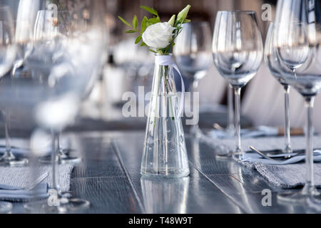 Transparentes Glas Vase mit Blumenstrauß vor Hintergrund der Tabelle Einstellung im modernen Restaurant. Wein und Wasser Gläser stehen in der Zeile auf Holz Stockfoto