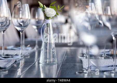 Transparentes Glas Vase mit Blumenstrauß vor Hintergrund der Tabelle Einstellung im modernen Restaurant. Wein und Wasser Gläser stehen in der Zeile auf Holz Stockfoto