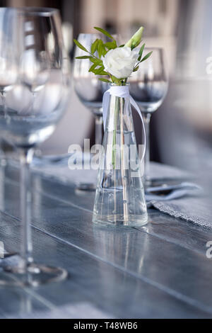 Transparentes Glas Vase mit Blumenstrauß vor Hintergrund der Tabelle Einstellung im modernen Restaurant. Wein und Wasser Gläser stehen in der Zeile auf Holz Stockfoto