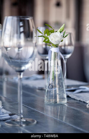 Transparentes Glas Vase mit Blumenstrauß vor Hintergrund der Tabelle Einstellung im modernen Restaurant. Wein und Wasser Gläser stehen in der Zeile auf Holz Stockfoto