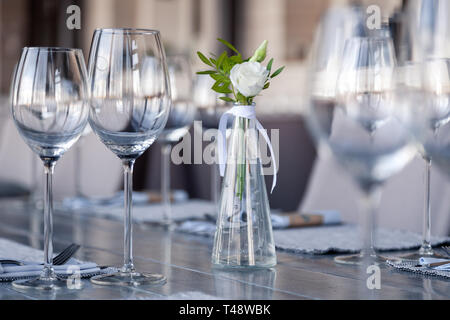 Transparentes Glas Vase mit Blumenstrauß vor Hintergrund der Tabelle Einstellung im modernen Restaurant. Wein und Wasser Gläser stehen in der Zeile auf Holz Stockfoto
