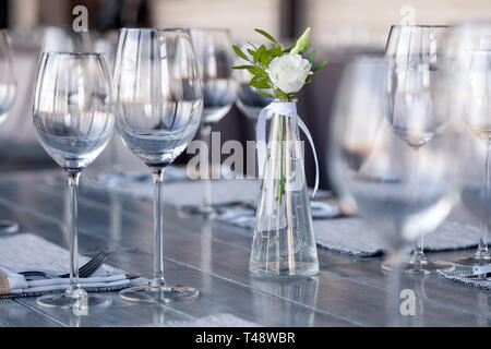 Transparentes Glas Vase mit Blumenstrauß vor Hintergrund der Tabelle Einstellung im modernen Restaurant. Wein und Wasser Gläser stehen in der Zeile auf Holz Stockfoto