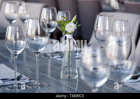 Transparentes Glas Vase mit Blumenstrauß vor Hintergrund der Tabelle Einstellung im modernen Restaurant. Wein und Wasser Gläser stehen in der Zeile auf Holz Stockfoto