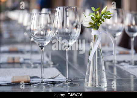 Transparentes Glas Vase mit Blumenstrauß vor Hintergrund der Tabelle Einstellung im modernen Restaurant. Wein und Wasser Gläser stehen in der Zeile auf Holz Stockfoto