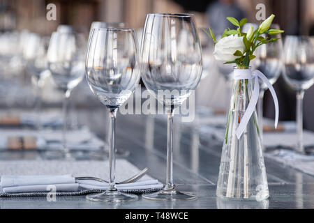 Transparentes Glas Vase mit Blumenstrauß vor Hintergrund der Tabelle Einstellung im modernen Restaurant. Wein und Wasser Gläser stehen in der Zeile auf Holz Stockfoto