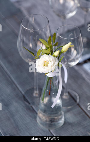 Transparentes Glas Vase mit Blumenstrauß vor Hintergrund der Tabelle Einstellung im modernen Restaurant. Wein und Wasser Gläser stehen in der Zeile auf Holz Stockfoto