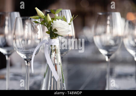 Transparentes Glas Vase mit Blumenstrauß vor Hintergrund der Tabelle Einstellung im modernen Restaurant. Wein und Wasser Gläser stehen in der Zeile auf Holz Stockfoto
