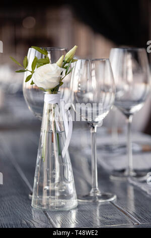Transparentes Glas Vase mit Blumenstrauß vor Hintergrund der Tabelle Einstellung im modernen Restaurant. Wein und Wasser Gläser stehen in der Zeile auf Holz Stockfoto