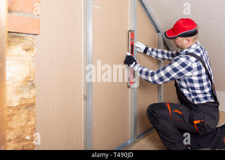 Man holding level against plasterboard, interior drywall. Attic renovation Stockfoto