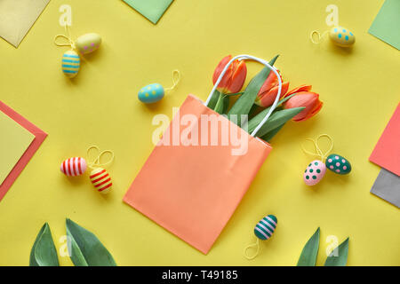 Ostern flach auf gelbem Papier. Bumch von orange Tulpen in Papiertüte, dekorative Ostereier, Geschenkkarten und Bunny Jahre aus Tulip verlässt. Stockfoto