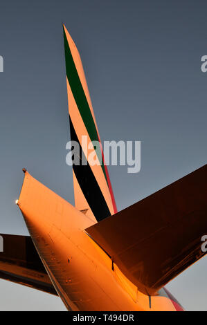 Ein Sonnenuntergang in der Nähe des Schwanzes ein Emirates Boeing 777 am Tor. Stockfoto