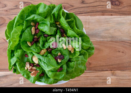 Leiter der frische Butter Kopfsalat mit in Scheiben geschnittenen Mandeln und getrockneten cranberry Salat Topper, in einer weißen Schüssel auf ein Holz Hintergrund Stockfoto