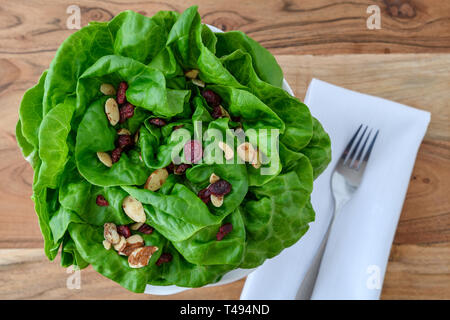 Leiter der frische Butter Kopfsalat mit in Scheiben geschnittenen Mandeln und getrockneten cranberry Salat Topper, in einer weißen Schüssel auf einem Holz Hintergrund, weiße Tuch Serviette und Metall f Stockfoto