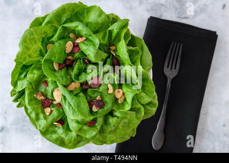 Leiter der frische Butter Kopfsalat mit in Scheiben geschnittenen Mandeln und getrockneten cranberry Salat Topper, in einer weißen Schüssel auf weißem und grauem Marmor Hintergrund, schwarze Tuch n Stockfoto