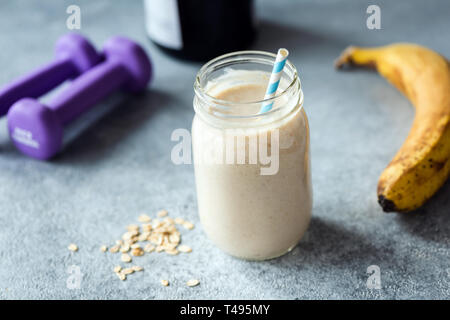 Protein Milchshake oder Smoothie mit Banane und Hafer auf konkrete Tabelle. Detailansicht, selektiver Fokus Stockfoto