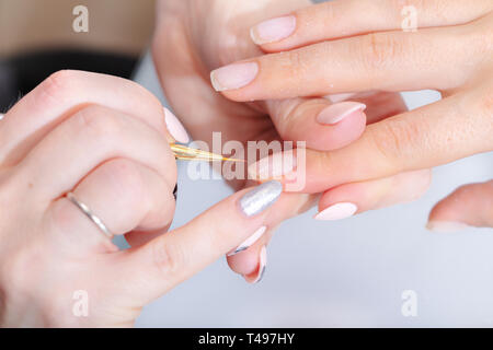 Die Hände der Meister der Hardware Maniküre und die Hände des Client close-up während der Anwendung von Lacken. Professionelle Nagelpflege, hell Stockfoto