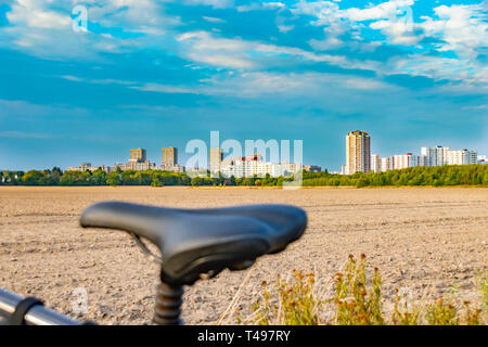 Blick über den Sattel eines Fahrrades. Im Hintergrund sehen Sie ein Feld und die unfocused Sat-Stadt der Gropiusstadt in Berlin-Neukölln. Stockfoto