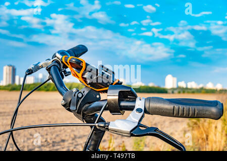 Blick über den Lenker eines Fahrrades. Im Hintergrund sehen Sie ein Feld und die unfocused Sat-Stadt der Gropiusstadt in Berlin-Neukölln. Stockfoto