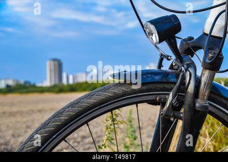 Blick über das Vorderrad eines Fahrrades. Im Hintergrund sehen Sie ein Feld und die unfocused Sat-Stadt der Gropiusstadt in Berlin-Neukölln. Stockfoto