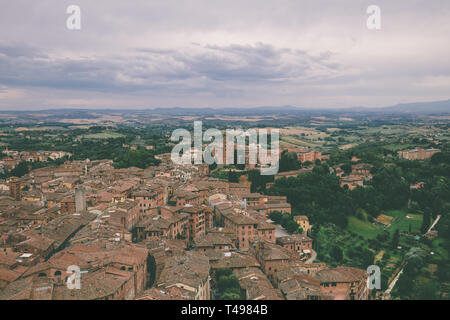 Panoramablick auf Siena Stadt mit historischen Gebäuden und weit weg die grünen Felder von Torre del Mangia ist ein Turm in der Stadt. Sommer sonnigen Tag und dramatische Stockfoto