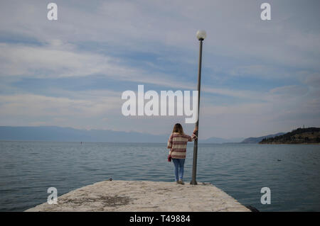 Ein stehendes Mädchen am Ende der Pier mit Blick auf die große Leere eines natürlichen See. Stockfoto