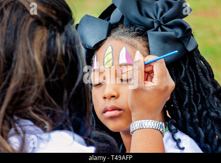 Ein Mädchen schließt die Augen wie ein Gesicht Maler Eye Shadow während einer Gemeinschaft Ostereiersuche am Langan Park, April 13, 2019 in Mobile, Alabama. Stockfoto