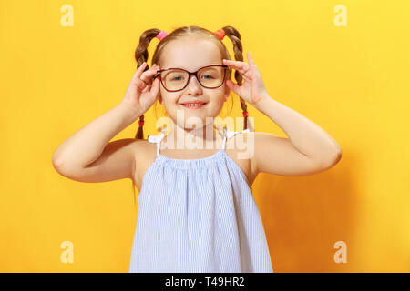 Porträt einer lustigen, kleinen Mädchen auf einem gelben Hintergrund. Vorschule Kind streckt Gläser. Stockfoto
