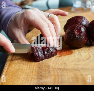 Eine Frau hacken Frische rote Beete für den Einsatz in einem Sprung auf einer hölzernen Schneidebrett in einer Küche Stockfoto
