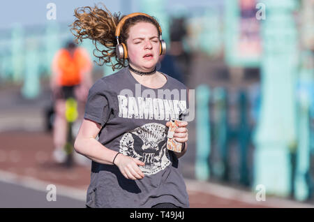 Vorderansicht einer jungen Frau joggen mit Haare fliegen in den Wind, das Tragen von Kopfhörern, die im Frühjahr in Großbritannien. Gesunde Lebensweise. Stockfoto