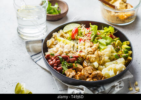 Vegetarisches Mittagessen. Brauner Reis mit Pilzen, Bohnen, Salat und hummus in einer schwarzen Platte, sauber eatind. Stockfoto