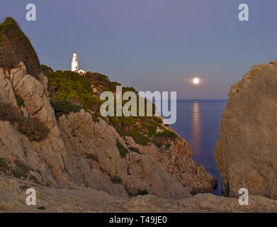 Weit de Capdepera Leuchtturm, Dämmerung, Abend, moonbeam am Meer mit Felsen und Bäumen, Cala Ratjada, Mallorca, Spanien. Stockfoto