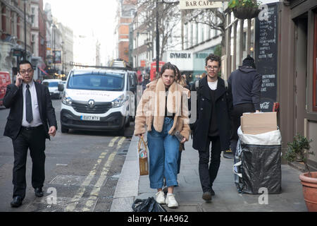 LONDON - Februar 17, 2019: ein Mädchen in einem fellimitat Mantel und Jeans zusammen mit einem jungen Mann mit Brille gehen Sie entlang der Straße Stockfoto