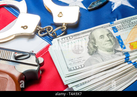 Konzeptionelle Foto der Kriminalität und Geld: Dollar, Handschellen und eine Pistole auf der amerikanischen Flagge Stockfoto