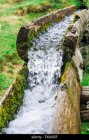 Wasser, Quelle des Lebens fließt Frisch und vom Berg ins Tal in einem hölzernen Kanal in der Natur reinigen Stockfoto
