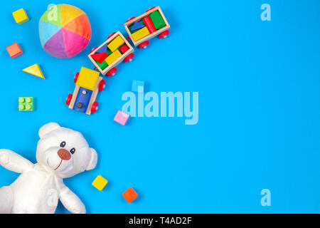 Baby Kinder Spielzeug Hintergrund. Weißer Teddybär, Holz- zug, bunte Bausteine auf blauem Hintergrund Stockfoto