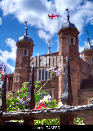 Das historische Guildford Großbritannien Frühling Blumen durch alte Geländer im Vordergrund und Kreuz von St. George flag gesehen auf Jacobean Abbot's Krankenhaus in Surrey UK Stockfoto