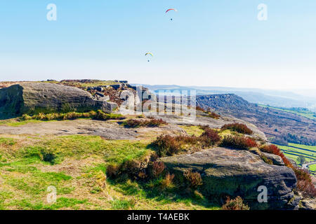 Zwei Gleitschirme fliegen über Curbar Edge, in The Derbyshire Peak District, auf einem dunstigen Frühlingstag. Stockfoto