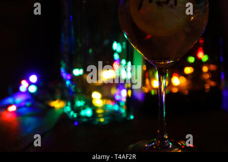 Nahaufnahme von Cocktail mit Zitronenscheiben und Eiswürfel und Flaschen (Schwerpunkt Glas stem) Stockfoto