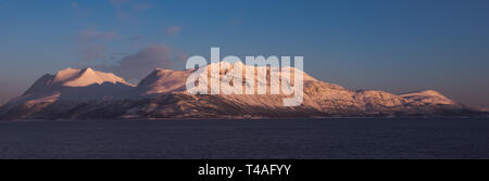 Blick von der Küstenlinie von Bakkejord, in der Nähe von Tromsø, Norwegen bei Sonnenuntergang. angezeigt Bergkette in der Ferne. März 2019. Stockfoto