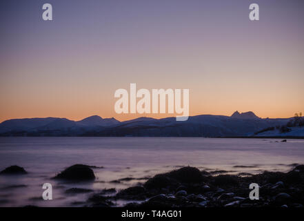 Blick von der Küstenlinie von Bakkejord, in der Nähe von Tromsø, Norwegen bei Sonnenuntergang. angezeigt Bergkette in der Ferne. März 2019. Stockfoto