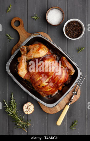 Gebratenes Huhn in einem rasting Zinn mit Zutaten und Carving Gabel auf einem dunkelgrauen Hintergrund Holz Stockfoto