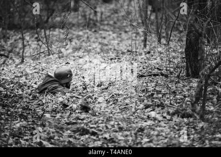 Re-Enactor in Mantel als Deutsche Wehrmacht Infanterie Soldat im Zweiten Weltkrieg versteckt im Hinterhalt im Herbst Wald gekleidet. Foto in den Farben Schwarz und Weiß Stockfoto