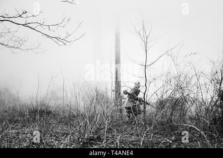 Re-Enactor in Mantel als Zweiter Weltkrieg russisch-sowjetischen Roten Armee Soldat im Nebel Rauch mit Maschinengewehr im nebligen Wald Boden gekleidet. Foto In Stockfoto