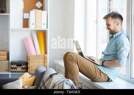 Junger Mann mit Laptop durch Fenster Stockfoto