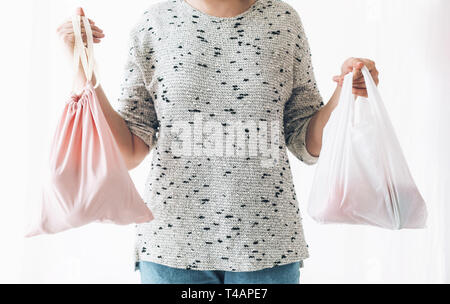 Verbot single use Kunststoff. Null Abfall shopping Konzept. Frau mit einer Hand Lebensmittel in wiederverwendbare eco Beutel und in anderen Gemüse in Kunststoff polyet Stockfoto