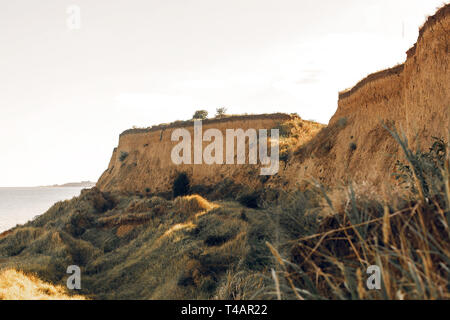 Wunderschöne Aussicht auf sandigen Felsen in der Nähe Meer Strand. Landschaft von Strand Klippe mit grünem Gras. Sommer Urlaub Konzept. Erkunden Sie interessante Orte Stockfoto