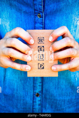 Frau Hände halten Kartonkarte mit Worten helfen durch schwarze Alphabet Briefmarken gemacht. Denim Hintergründe. Stockfoto