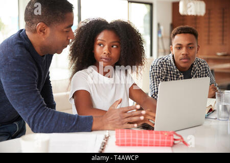 Im mittleren Alter schwarzer Mann, der seine Kinder im Teenageralter helfen, ihre Hausaufgaben mit Laptop Stockfoto